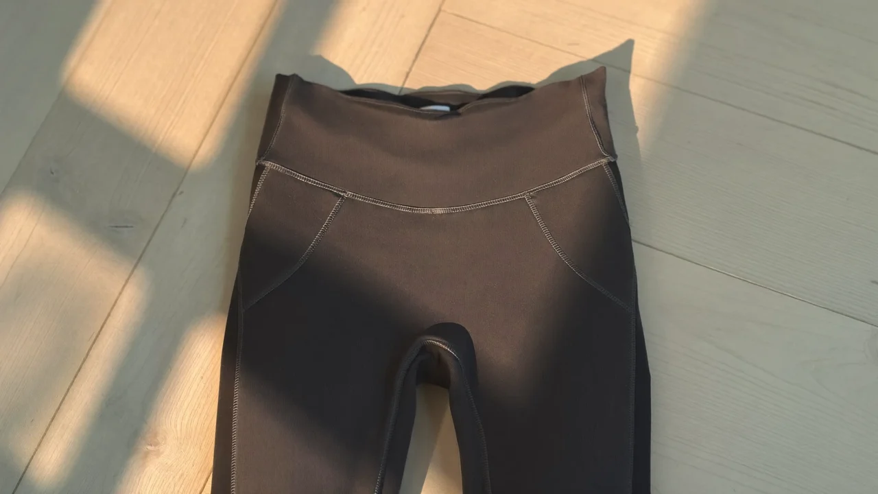 Anthrazitfarbene Kompressions-Leggings flach auf hellem Holzboden im Fensterlicht