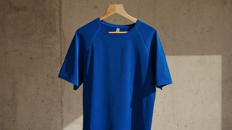 Kobaltblaues Laufshirt auf einem Holzbügel vor einer Betonwand