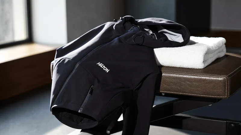 Marineblaue Softshelljacke mit Kapuze auf einer Trainingsbank neben einem Handtuch