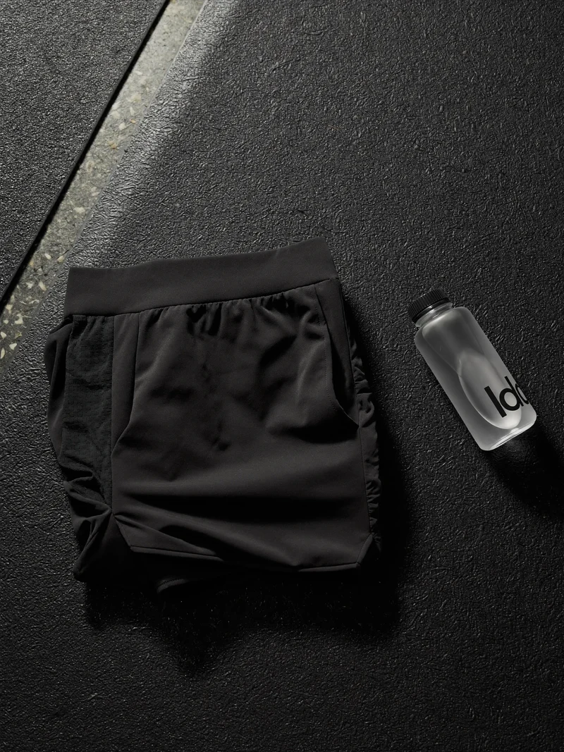 Schwarze Trainingsshorts mit Mesh-Einsätzen auf einer Gummimatte neben einer Trinkflasche